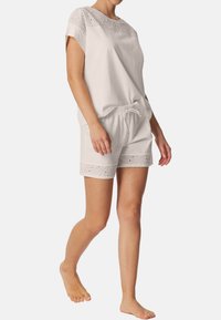 Vit bomullsloungewear-set bestående av en kortärmad topp med broderade detaljer och matchande shorts med broderade fållar och dragsko i midjan.