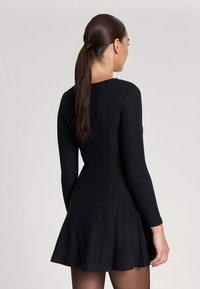 Abito nero a coste con maniche lunghe, corpino aderente e orlo svasato. Presenta un colletto tondo e un tessuto testurizzato per un tocco di dettaglio in più.