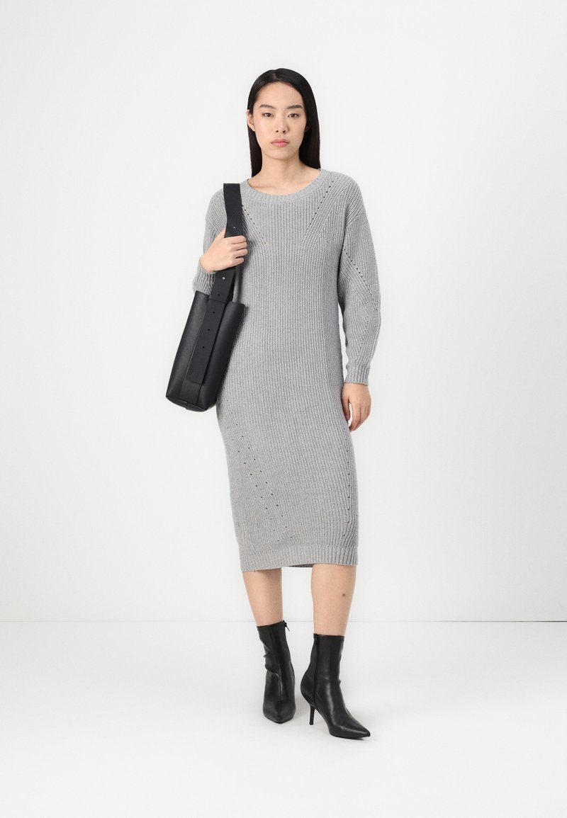 Szara dzianinowa sukienka z długimi rękawami, prążkowaną fakturą i prostym krojem. Połączona z czarnymi botkami za kostkę i czarną torbą typu tote.
