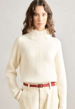 Chunky geribde gebreide turtleneck trui in crème, gecombineerd met een rode leren riem. Beschikt over lange mouwen en een comfortabele fit.