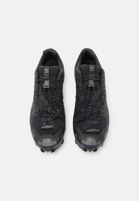 Chaussures de sport noires avec une tige en mesh durable, des semelles en caoutchouc texturé et une semelle extérieure agressive. Dotées d'un système de laçage et d'accents de branding discrets.