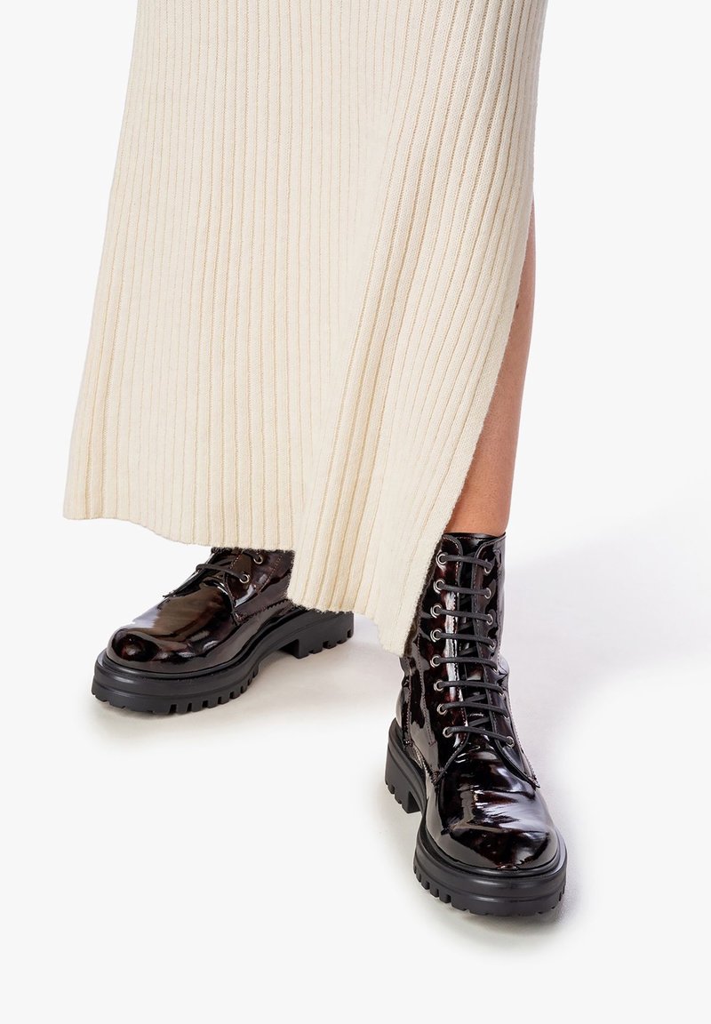 Bottes de combat noires brillantes à lacets avec semelles épaisses portées avec une jupe côtelée crème présentant des fentes latérales.