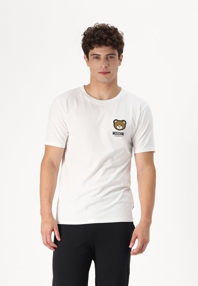 Biała koszulka z krótkim rękawem, wykonana z miękkiego materiału, z grafiką brązowego niedźwiedzia i napisem "MOSCHINO" na lewej piersi.