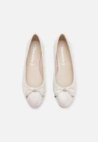 Ballerines beiges en matériau synthétique lisse, avec un bout arrondi et un nœud orné d'un petit cristal.