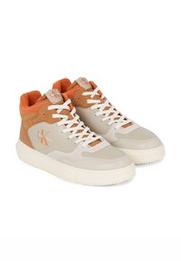 Beige nahkahigh-top-tennarit, joissa on ruskeat ja oranssit yksityiskohdat. Varustettu valkoisilla nauhoilla, pehmustetulla nilkkaremmillä ja teksturoidulla kumipohjalla.