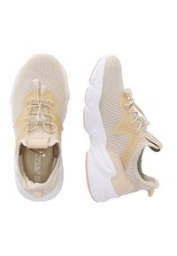 Baskets de sport beiges avec une tige en mesh, des lacets élastiques et une semelle blanche épaisse ornée de motifs texturés sur les côtés.