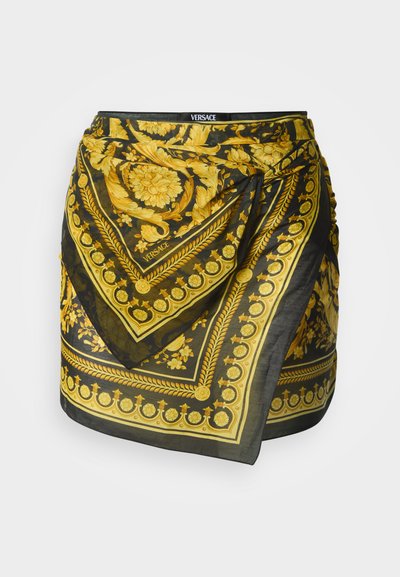 Čierna hodvábna zavinovacia sukňa s motívom zlatej barokovej vzory, s dekoratívnym lemovaním a logom Versace, vytvárajúca luxusný vizuálny kontrast.