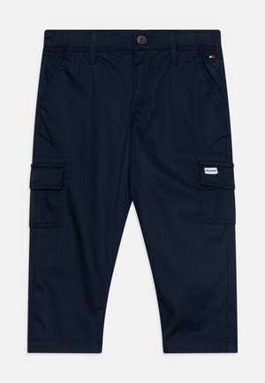 Pantalon cargo bleu marine avec poches avant, poches latérales à rabat, passants de ceinture et une petite étiquette tissu de la marque sur la poche droite.
