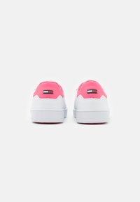 Sneakers bianchi con finitura liscia, dettagli rosa sul tallone e logo sul retro. Presentano una suola in gomma con scanalature testurizzate.