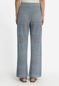 Ljusblå virkade byxor med vida ben, prydda med horisontella mönster och ett texturerat midjeband. Det öppna vävdesignen ger genomsiktlighet genom tyget.