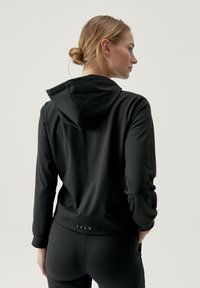 Hoodie atletico nero con una vestibilità aderente, maniche lunghe e un cappuccio spazioso. Presenta una semplice cucitura e una lieve texture sul tessuto.