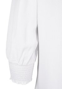 Manchette en tissu blanc texturé avec un poignet élastique froncé créant une apparence bouffante.