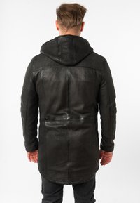 Zwarte leren jas met capuchon, met een gladde textuur, een verlengd achterpand en contrasterende stiksels.