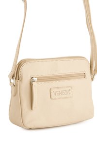 Beige Leder Umhängetasche mit verstellbarem Riemen, ausgestattet mit einem Reißverschluss-Hauptfach und einer Vordertasche. Prägiertes Markenlogo auf der Vorderseite.