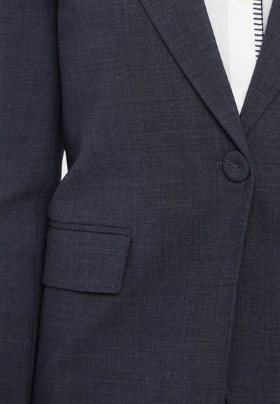 Blazer navy in tessuto texturizzato con chiusura a un bottone e tasca applicata. Vestibilità tailored con revers strutturati.