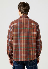 Camicia a scacchi marrone con finitura texturizzata; presenta strisce blu, arancioni e bianche, polsini abbottonati e orlo dritto.