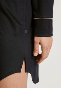 Abito a maniche lunghe blu navy con orlo curvo, spacco laterale e piping chiaro sulle maniche. Tessuto morbido e testurizzato visibile.