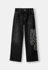 Musta farkkubahka, jossa on rento leikkaus ja vasemmassa jalassa suuri valkoinen "RACE RUNNER" -grafiikka sekä erivärinen ommel vyötäröllä.