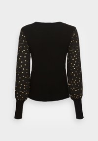 Haut noir à manches longues avec des manches transparentes à pois dorés et des poignets côtelés ajustés, vu de dos sur fond blanc.