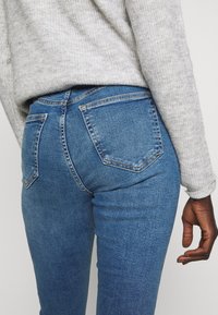 Blue denim jeans with a slim fit, five-pocket design, light fading, and contrasting stitching. Worn with a gray knit sweater.