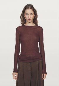 Langärmliges Oberteil aus burgunderfarbenem, transparentem Stoff mit rundem Ausschnitt. Lockere Passform mit geradem Saum, kombiniert mit hochtaillierten braunen Hosen.