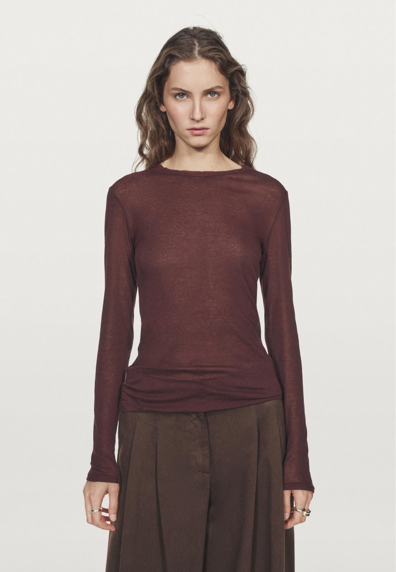 Langärmliges Oberteil aus burgunderfarbenem, transparentem Stoff mit rundem Ausschnitt. Lockere Passform mit geradem Saum, kombiniert mit hochtaillierten braunen Hosen.