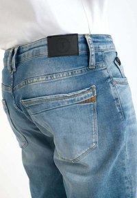 Lichtblauwe denim jeans met een medium-rise taille, voorzien van een zwarte leren patch aan de achterkant, details op de zakken en een vervaagde textuur.