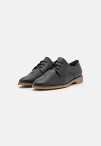 Chaussures en cuir noir à finition lisse, présentant un bout arrondi, des coutures minimales et une semelle en bois marron clair. Design classique à lacets.