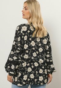 Blusa nera con fiori crema, maniche a palloncino e accenti testurizzati. Vestibilità comoda, tessuto leggero e intricato motivo floreale.