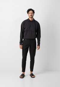 Svart hettegenser med glidelås og frontlomme, sammen med svarte slim-fit cargo bukser med sidelommer, og svarte sandaler.