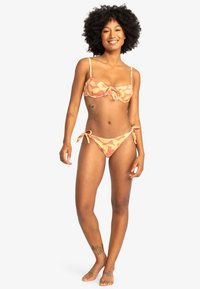 Bikini set in zachte perzik-oranje stof met bloemmotieven. Top met verstelbare bandjes en een strik aan de voorkant; broekje met zijstrikjes.