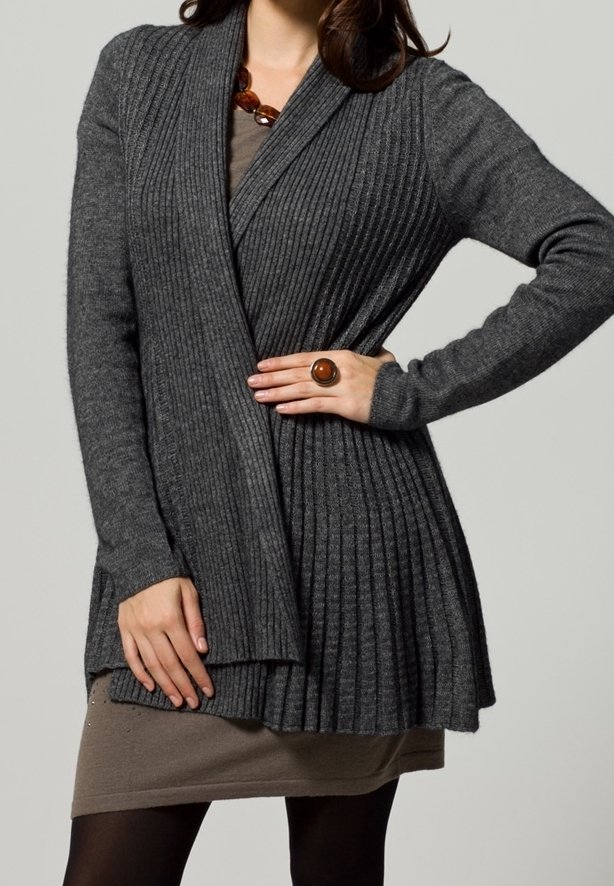 Cardigan grigio a coste con fronte drappeggiato e design plissé. Materiale in maglia morbida, abbinato a un vestito beige e a un anello circolare marrone.