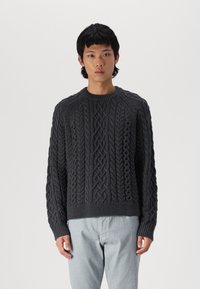 Pulover tricotat de culoare gri închis, cu un design texturat de cabluri, guler rotund și tiv rib, asortat cu pantaloni de culoare deschisă.