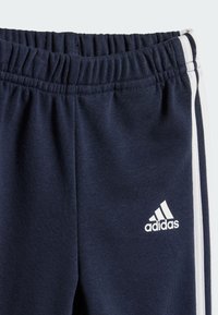 Pantaloni sportivi Adidas blu navy con strisce laterali bianche. Dotati di vita elastica e texture morbida. Logo visibile in basso a sinistra.