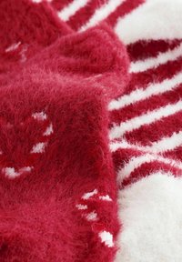 Piros-fehér texturált kötött anyag bolyhos fonallal, csíkok és apró részletek kontrasztos színű mintázatváltozataival.