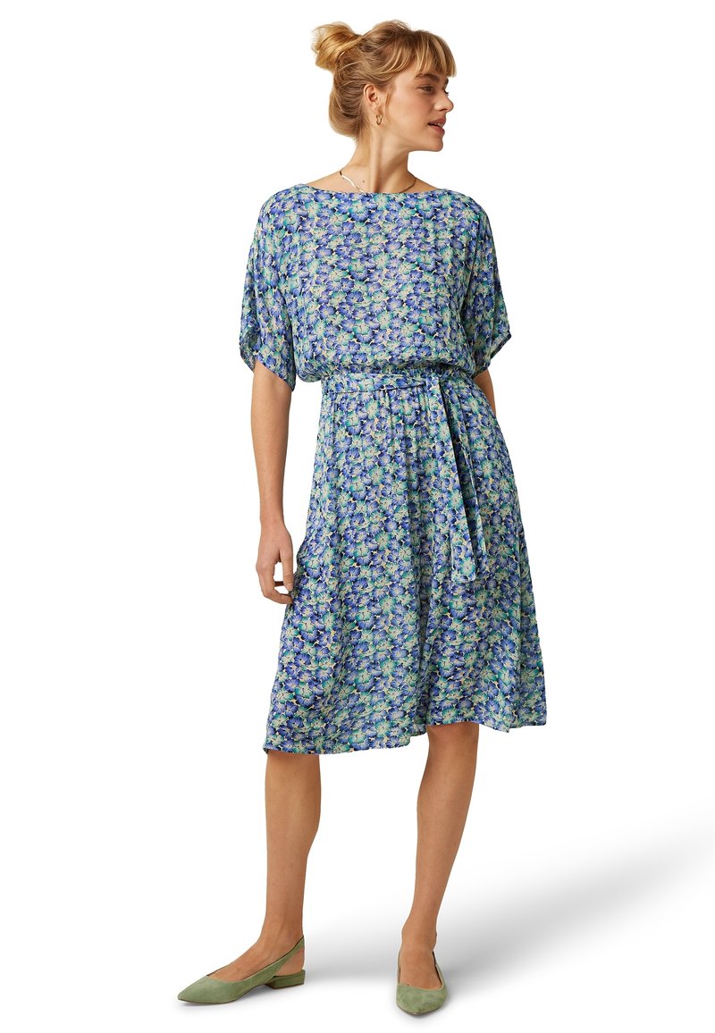 Vestido con estampado floral en tonos azules y verdes, mangas cortas, cintura elástica y cinturón. Tejido suave con un diseño fluido, largo hasta la rodilla.