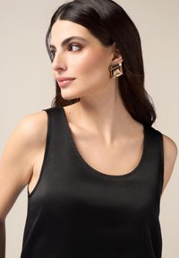 Top in satin nero con scollo a barca, abbinato a un grande orecchino geometrico dorato, che mette in risalto texture lucide e un design audace.