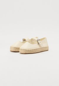 Espadrilles de color crema con suela de yute trenzado, que presentan una punta redondeada y una única correa ajustable a lo largo del empeine.