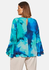 Blusa fluida con un vivace motivo ad acquerello blu e teal, tessuto trasparente, maniche a ruffle e dettaglio di apertura a chiave nella parte posteriore.