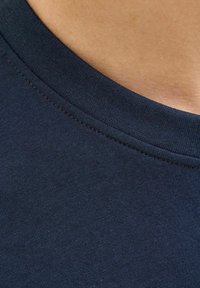 Tricou din bumbac de culoare bleumarin cu guler rotund. Prezintă o textură netedă și cusături vizibile pe marginea gulerului. Prim-plan al detaliilor materialului.