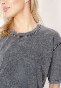 Szary bawełniany t-shirt z okrągłym dekoltem, opuszczonymi ramionami oraz dużym okrągłym logo "A" nadrukowanym z przodu. Miękka tekstura.