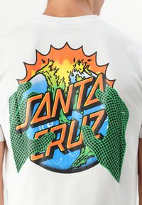 Witte T-shirt met een kleurraf grafiek van groene handen die de aarde vasthouden, omgeven door een heldere oranje zonnestraal en de tekst "SANTA CRUZ".