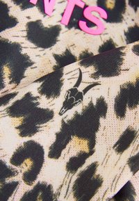 Tissu à imprimé léopard avec des taches noires sur un fond beige, accompagné d'un texte rose vif et d'un motif détaillé de crâne de chèvre noir.