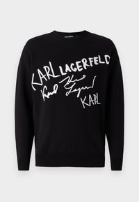Black sweater featuring white embroidered text reading "KARL LAGERFELD" and a signature design. Simple crew neck and long sleeves.