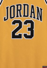 Żółta siatkowa koszulka do koszykówki z napisem "JORDAN" w czarnych literach oraz "23" w czerni, z białym obszyciem. Koszulka ma również czarno-białą konstrukcję przy dekolcie.