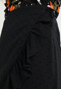Svart kjol med subtil prickig struktur, med volangkant och knytning på sidan, tillverkad av lättviktig tyg.
