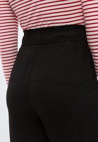 Μαύρο παντελόνι με υφή, με ελαστική μέση και πλαϊνής τσέπης, συνδυασμένο με κόκκινο και λευκό ριγέ τοπ.