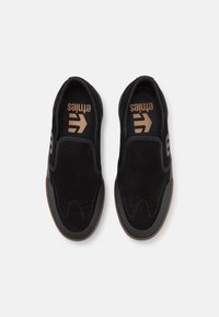 Černé nazouvací boty z semiše a síťoviny s hnědou gumovou podrážkou a perforovanými detaily. Logo je zobrazeno v kontrastních barvách.