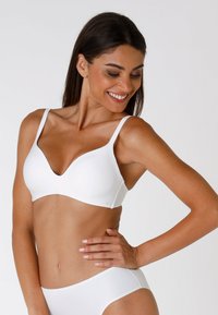Soutien-gorge bianco con scollatura profonda, spalline regolabili, texture liscia e senza cuciture visibili. Indossato con culotte bianche coordinate.