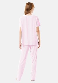 Conjunto de pijama rosa que incluye una camiseta de manga corta y pantalones largos, confeccionado en una suave tela con una textura sutil y un corte relajado.